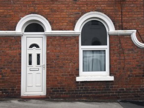 White front door and window of a typical old brick british terraced house with white decorative