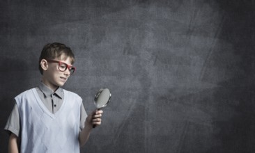 Cute boy looking through magnifying glass against blackboard background