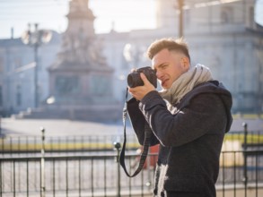 Handsome young male photographer taking photograph with professional photo camera hanging from his