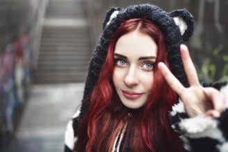 Close up portrait of cheerful playful girl, who is gesturing peace sign and smiles. She is wearing
