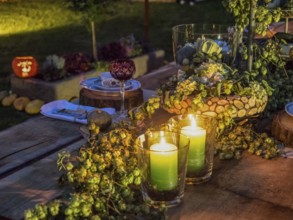 Two green candles glowing on a decorated outdoor table, surrounded by flowers and other decorative