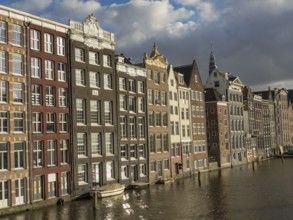 Row of historic canal houses on the waterfront with reflection and blue sky with clouds, amsterdam,