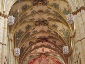 The interior of a church with ornate frescoes on the vaulted ceiling and decorative Gothic style