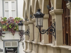Historic lanterns hanging on the wall of a building with arches and plants in the city, la palma,