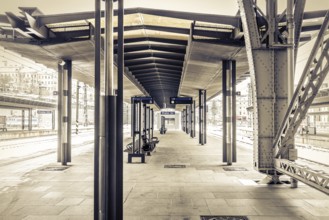Covered platform in an empty modern railway station in sepia colour with striking metal structure,