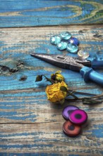 Beads, pliers, and other needlework accessories on outdated turquoise wooden background