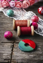Beads and spool of thread, piece of lace on textured wooden background