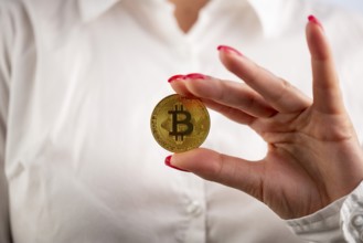 Virtual cryptocurrency money Bitcoin golden coin in the left hand of a woman with red nail polish.