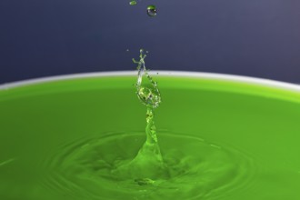 A drop of water forms a splashing sculpture on green liquid, water droplets, collision, high-speed