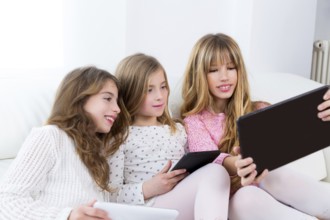 Three kid sister friends girls group playing together with tablet pc on white sofa