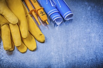 Yellow electrical tester safety gloves blue construction drawings on metallic background