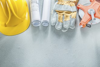 Safety gloves hard hats blueprints measuring tape on concrete background
