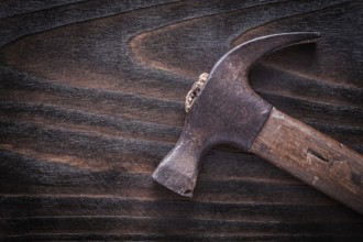Rusty metal claw hammer with wooden handle on vintage dark wooden board construction concept