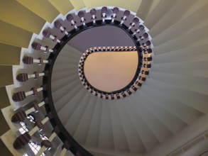 A looking upwards view of an elegant spiral staircase with wooden bannisters in elegant shades of