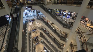Customers in trade centre riding escalators. View from upper to lower floor. Shopping mall of