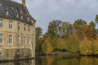 Historic castle on the shore of a lake with colourful autumn trees in the background, Borken,