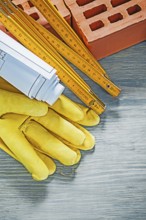 Composition of red bricks protective gloves blueprints wooden meter on wood board bricklaying