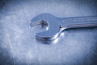 Stainless spanner wrench on scratched metallic background top view construction concept