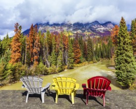 Scenic autumn in the Rockies of Canada. Three deck chairs stand over the forest and river.