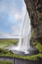 Sunny day in Iceland. Seljalandsfoss waterfall in July. Large rainbow decorates a drop of water.