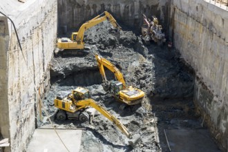 Excavators dig at a construction site of a street and a subway. Baggers transport dirt to a higher