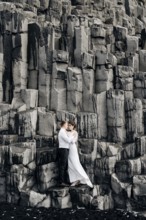 A wedding couple stands on a wall of stone pillars. The bride and groom are hugging on basalt