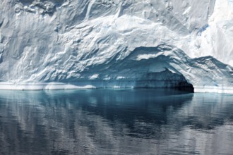 A large iceberg with a small cave is reflected in the calm, reflective water, icebergs in the