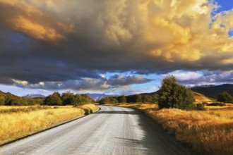The huge cloud lit yellow-orange rays of sunset. Gravel road through the Patagonian steppe