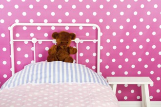 Girls bedroom with pink wall paper and stuffed bear
