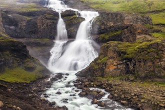 Powerful streams of cascade falls with a roar break against cold rocks. Cold and rainy July in