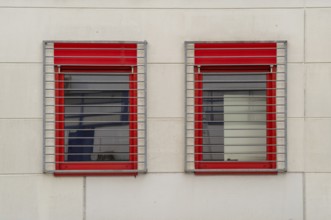 Two windows with red frames and metal grilles restrict the view outside