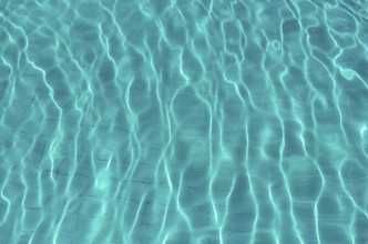 Waves on the light of the pool water. Swimming pool with blue water. Water surface texture. View