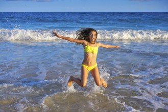 Bikini teen girl jumping happyt in Caribbean sunset beach splashing shore