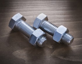 Threaded bolts and nuts on wooden surface construction concept