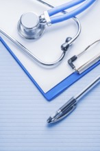 Ballpoint pen and stetoscope with clipboard on blue background medical concept