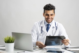 Handsome doctor looking at x-ray scan. Happy physician in white coat with stethoscope sitting at