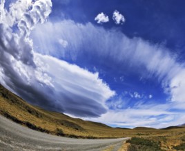 Gray dirt road in the Chilean national park to Torres del Paine. Improbable form the clouds created