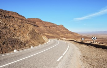 Kurve auf Asphaltstraße, kleine Atlas Berge und niedrige Büsche beide Seiten, klare Himmel über -
