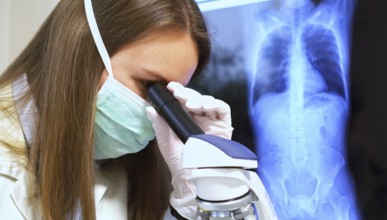Scientist in medical mask in laboratory. Chest x-ray film on background