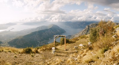 Simple wooden arch decorated with flowers stands on top of a mountain overlooking the valley.