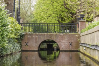 Small canal with a brick arch bridge and lush vegetation along the banks, den haag, the netherlands