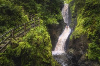 Spectacular wooden boardwalk on the hill with a view on tall waterfall and river in majestic