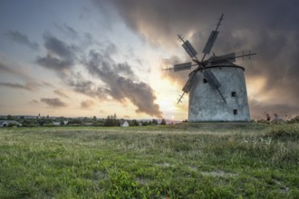 Windmill with wooden sails in a landscape with fields. Meadows and flowers appear in the sunset.