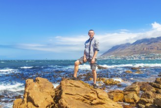 Male model tourist traveler at False Bay rough coast landscape with boulders waves and mountains