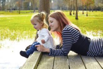 Daughter and mother playing together in the park lake pier