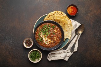 Traditional Indian Punjabi dish Dal makhani with lentils and beans in black bowl served with naan