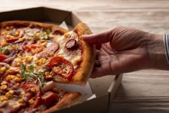 Human caucasian hand takes slice of large pizza from carton box on white wooden table
