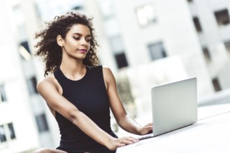 Young attractive Mixed-race girl with beautiful afro hair who is smiling looking at her laptop