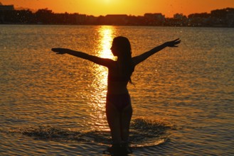 Girl silhouette at beach sunset open arms standing