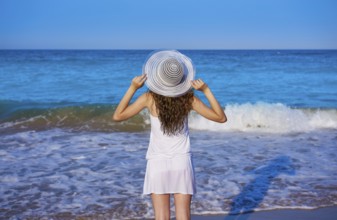 Girl with beach hat in sea open arms with summer white dress